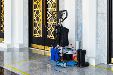 Floor polishing machine and cleaning supplies sit near a marble entrance with decorative gold...