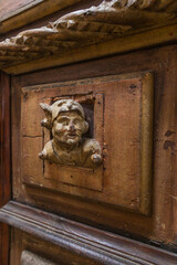 A weathered wooden panel featuring a carved bust of a whimsical figure with horns