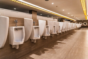 A row of modern white urinals in a spacious public restroom, with a clean tile floor, is...
