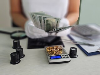 Holding cash while weighing gold jewelry on a digital scale in a monetary transaction concept