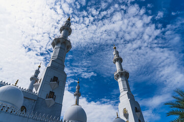 Low angle view of the Sheikh Zayed Mosque's white minarets and domes against a bright blue, cloudy...
