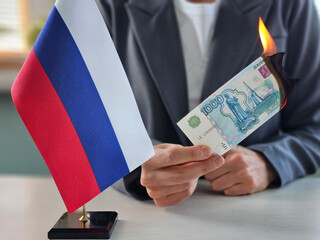 Individual burns ruble banknote beside Russian flag in protest during daylight hours concept