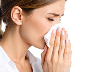 Young woman blowing nose into white tissue suffering from cold, flu, allergies or seasonal illness symptoms