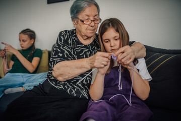 Grandmother teaching granddaughter to knit on sofa