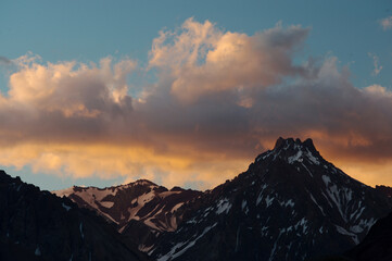 A night view of snowy mountains with clouds at sunset. The clouds and sky turn a magnificent golden color as the sun sets.