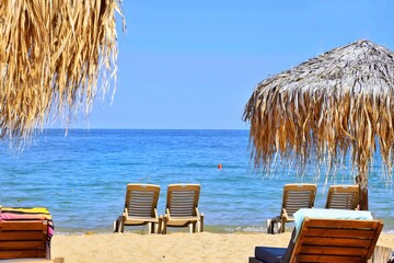Sun loungers and straw umbrellas on the beach by the sea. Seaside vacation concept.