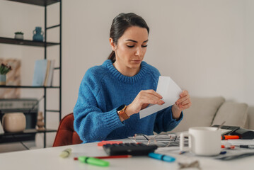 Woman opening envelope while calculating domestic bills at home office