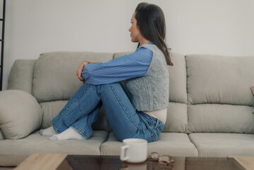 Sad young woman sitting on sofa at home thinking with a cup of coffee nearby