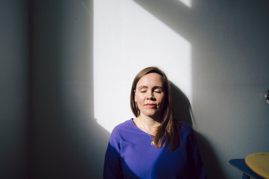 Woman enjoying sunlight indoors with a calm expression