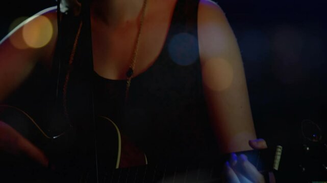 Camera zooming out showing teen singer strumming singing into mic for music show with bokeh lights