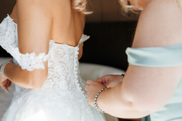 Bridesmaid helps the bride fasten the buttons on the wedding dress on the back close-up. Dressing...