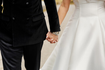 Bride and groom holding hands while walking down the road. Close-up of hands of happy wedding...