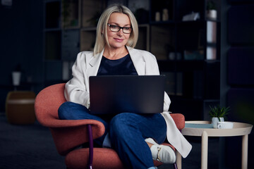 Smiling businesswoman using laptop sitting on chair in office