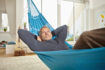 Man relaxing in a blue hammock indoors in a modern loft living room
