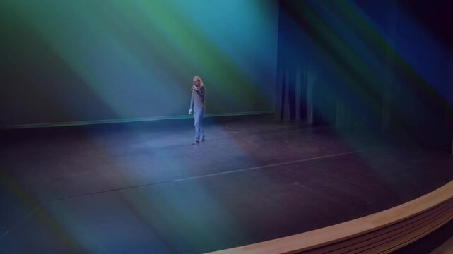 Singer entering empty stage and initiating music performance, moving under aqua green light beams