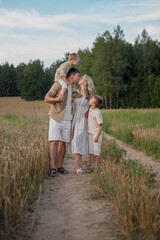 The family is standing on a wheat field, with parents hugging and kissing each other affectionately, and children looking at their parents with happiness. 