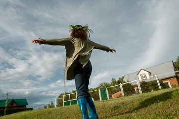 Woman with flower wreath spinning in green summer meadow, photographed from behind. Concept of...