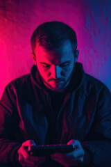 Bearded man intensely focused on playing a portable console, surrounded by deep blue and magenta neon light gradients, wearing dark clothing in a dim space