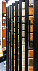 Obraz premium Close-up of wall tile samples displayed on a rack in a showroom, showing various textures and colors like orange and beige. Modern interior design concept.