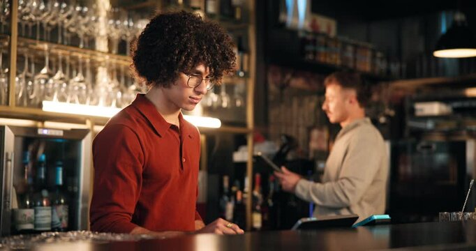 Bartender, man and tablet at pub for stock take, inspection and inventory checklist at small business. Trainee, bar manager and digital tech with app for menu, POS system and hospitality review