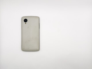 A white cell phone is laying on a white surface. copy space, flay lay, top view. The back of the phone is missing. The phone is not in use