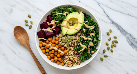  Colorful vegan Buddha bowl with quinoa, avocado, chickpeas, kale, and tahini dressing. Top-down view on marble table