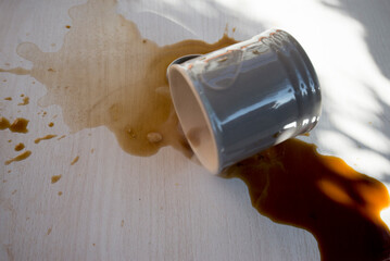 A cup of coffee on a wooden table with spilled coffee and caramel