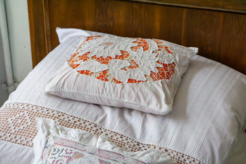 Pillow with embroidered doily on white lace bedding in a vintage, rustic interior.
