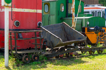 Historic narrow-gauge mining train with a tipping wagon, displayed on tracks next to colorful locomotives