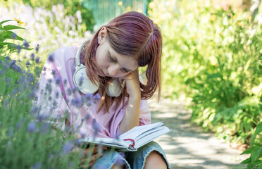 Young girl reading a book in a garden with headphones around her neck