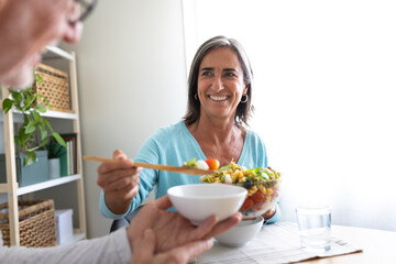 Woman serving pasta salad to husband. Mature married couple having meal together at home dining table