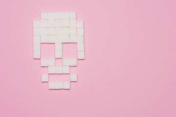 Still life concept of white sugar cubes forming skull on pink background with copy space
