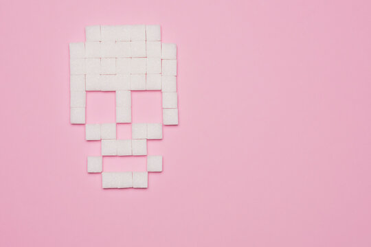 Still life concept of white sugar cubes forming skull on pink background with copy space
