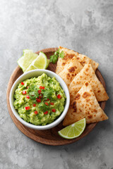 A bowl of guacamole sits on a wooden plate with tortilla chips