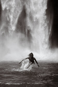 Young woman running through waterfall spray in Bali jungle pool