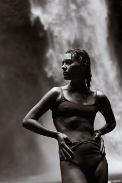 Woman standing confidently in front of waterfall, black and white