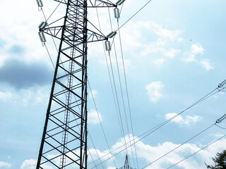 Tall electrical transmission tower against bright blue sky with clouds