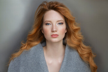 Formal portrait of beautiful young woman with wavy, long red hair against gray background
