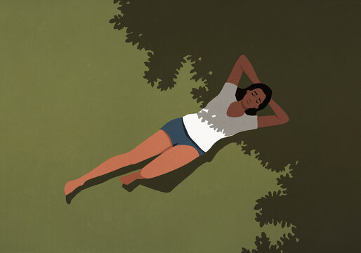 View from above of serene woman in shorts and t-shirt laying in sunlight and shadow in summer grass

