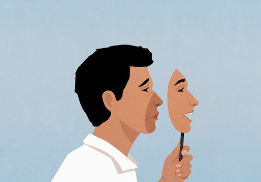 Profile of frowning man holding happy mask over face against blue background
