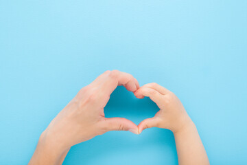 Heart shape created from little son and young mother hands on blue table background. Pastel color....