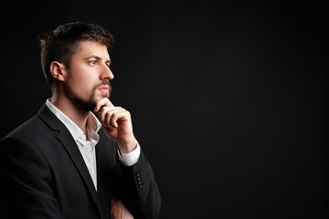 Man in a business suit contemplating ideas against a dark background in a studio setting