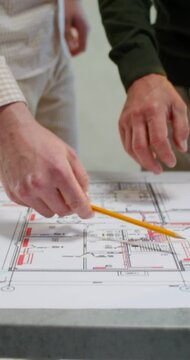 Two men are discussing a house construction project. They are talking standing next to a table in an unadorned room
