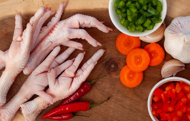 Raw chicken feet on wooden board with ingredients for cooking.