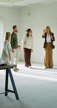 The realtor shows the house to a family with children. They walk around the room without decoration