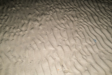Close-up view of wet beach sand at night, showing natural ripple patterns left by the receding tide under low light