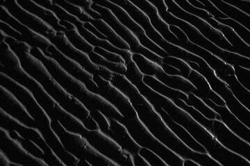 Dramatic black and white photo of beach sand ripples at night, highlighting textures and shadows...
