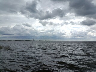 Rekyva lake during sunny day. Sunny day with white and gray clouds in sky. Wavy lake. Horizon over...