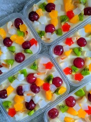Colorful fruit pudding in plastic containers, topped with grapes, kiwi, oranges, strawberries,...