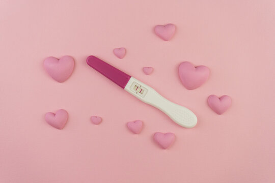 Positive Pregnancy Test with Pink Hearts on Pastel Background – Concept of Love, Expecting Baby, and Maternity - Powered by Adobe